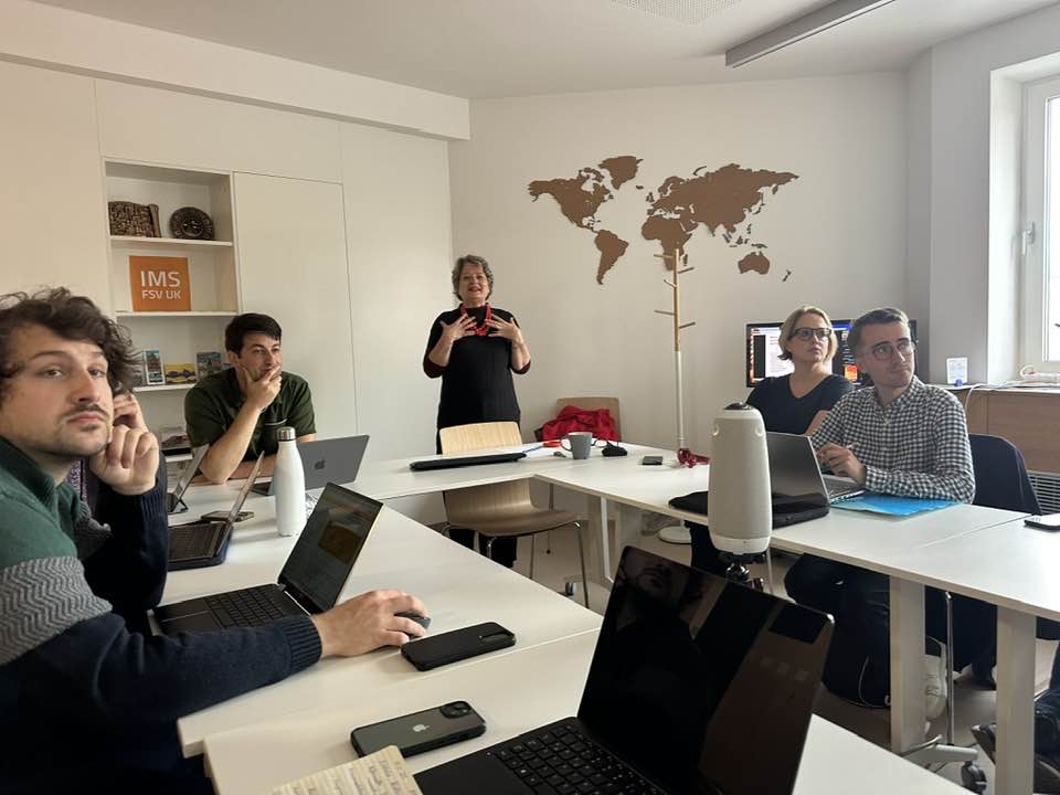 panel of men and women in a discussion facing a projector with their laptops on the table.