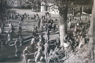 A group of people in military-style clothing gathered in an open outdoor area with trees and buildings in the background