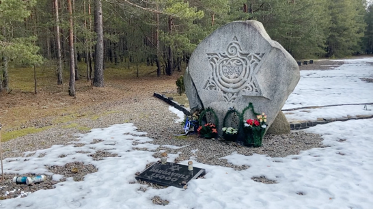 Stone monument with a Star of David engraving and floral tributes in a snowy forest clearing