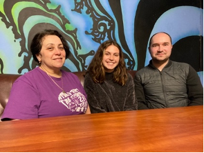 Three people sitting behind a wooden table in front of a colorful wall mural