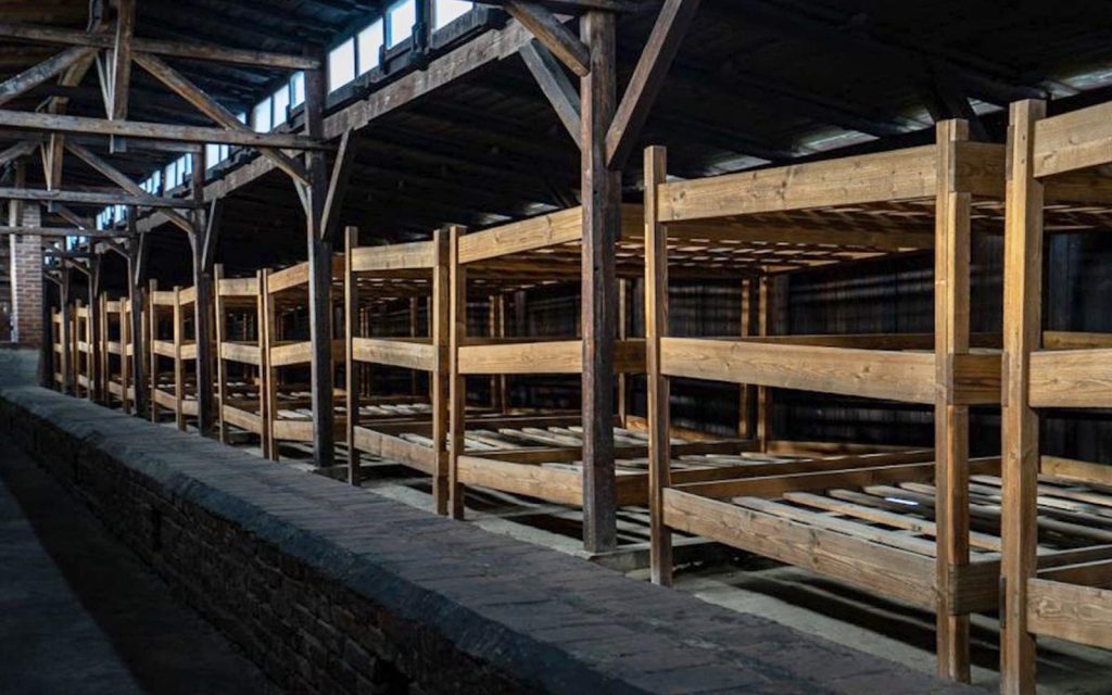 Rows of multi-tiered wooden bunk beds in a large, dim warehouse-style room with exposed beams
