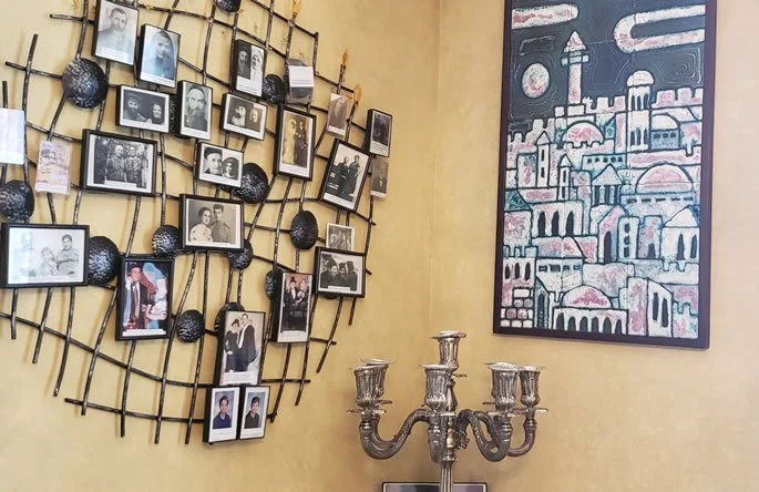A wall featuring a metal grid display of framed photographs and a painting of a city skyline with domes and minarets